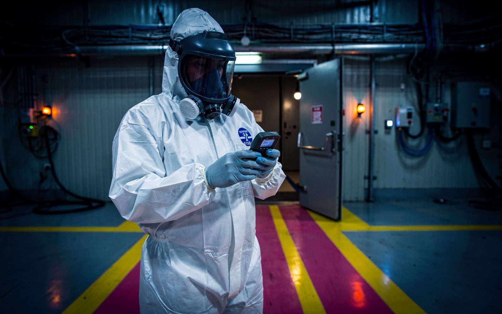 Technicien en radioprotection en tenue blanche contrôlant un dosimètre à l'entrée d'une zone contrôlée